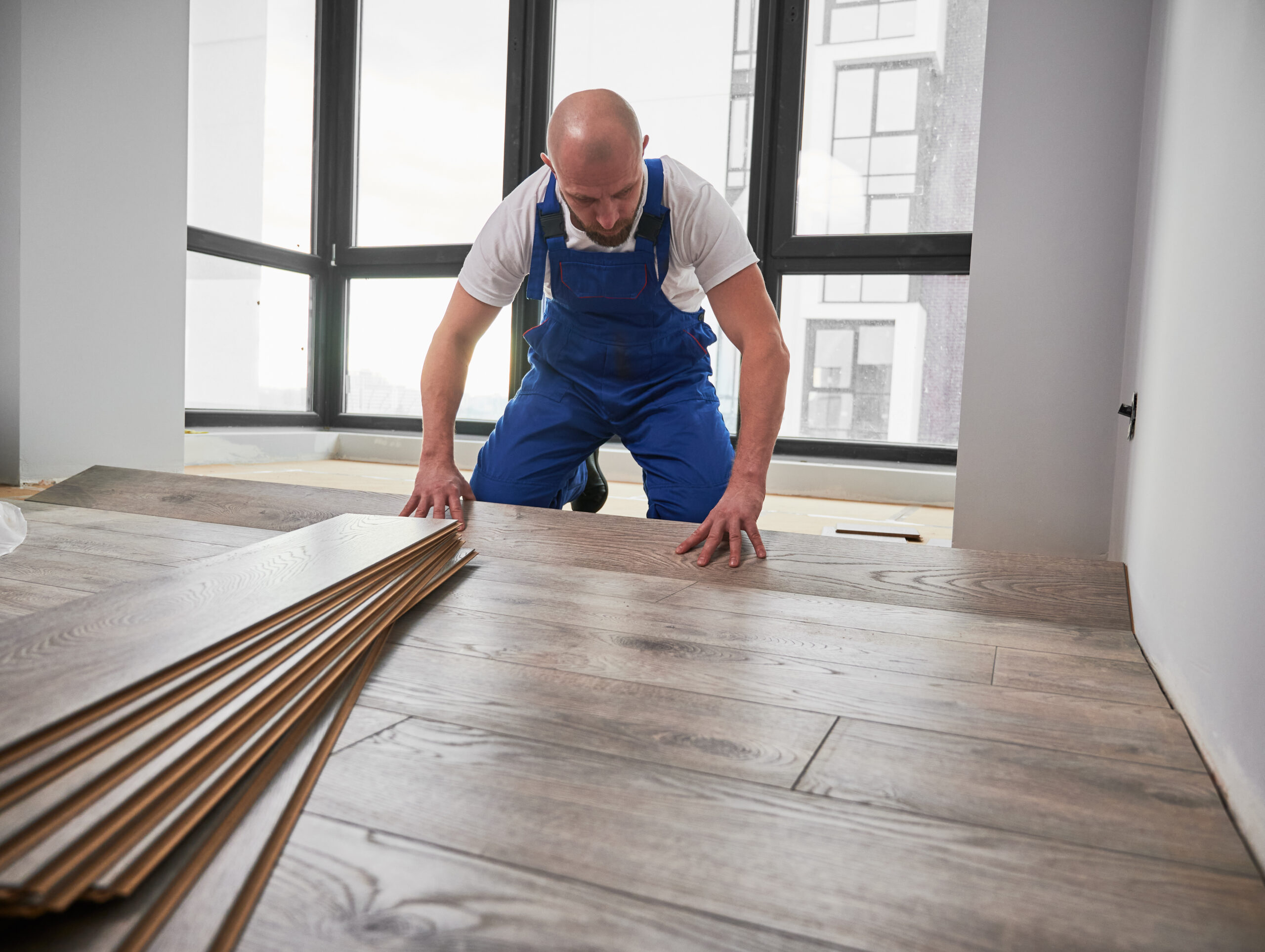 Man installing laminate flooring at home during renovation.